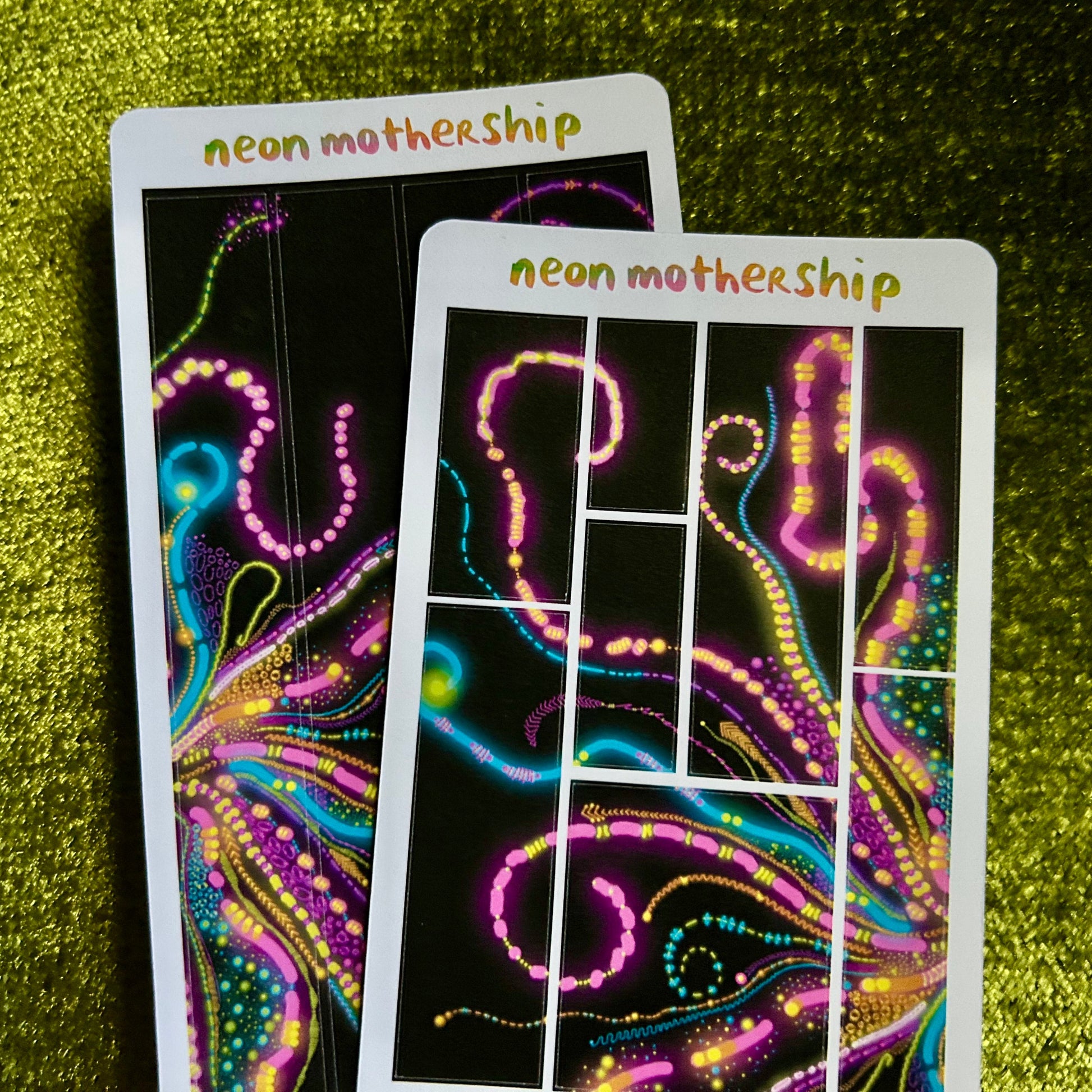 Two neon motherShip sticker sheets on a green textured background