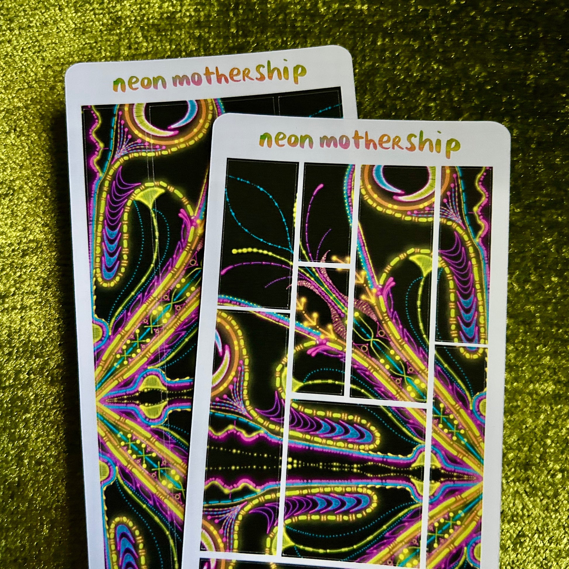Two neon 'neon mothership' sticker sheets on a green textured surface