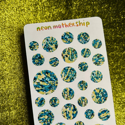 Sheet of round, multicolored stickers with 'neon motherShip' branding on a green textured background.