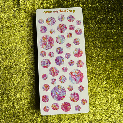 Sheet of colorful circular stickers on a green textured surface
