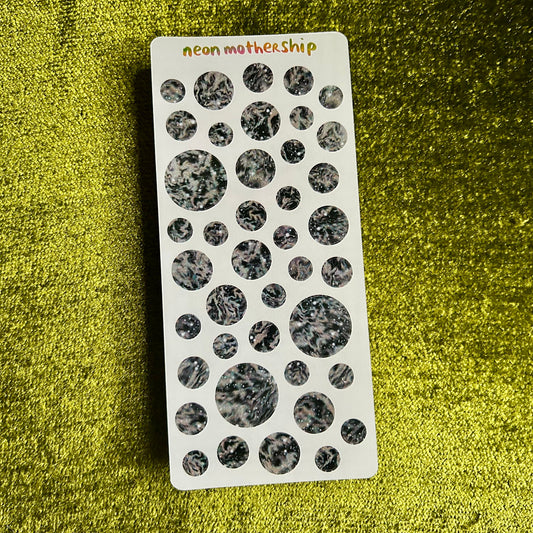 Sheet of black and white circular stickers on a green textured surface