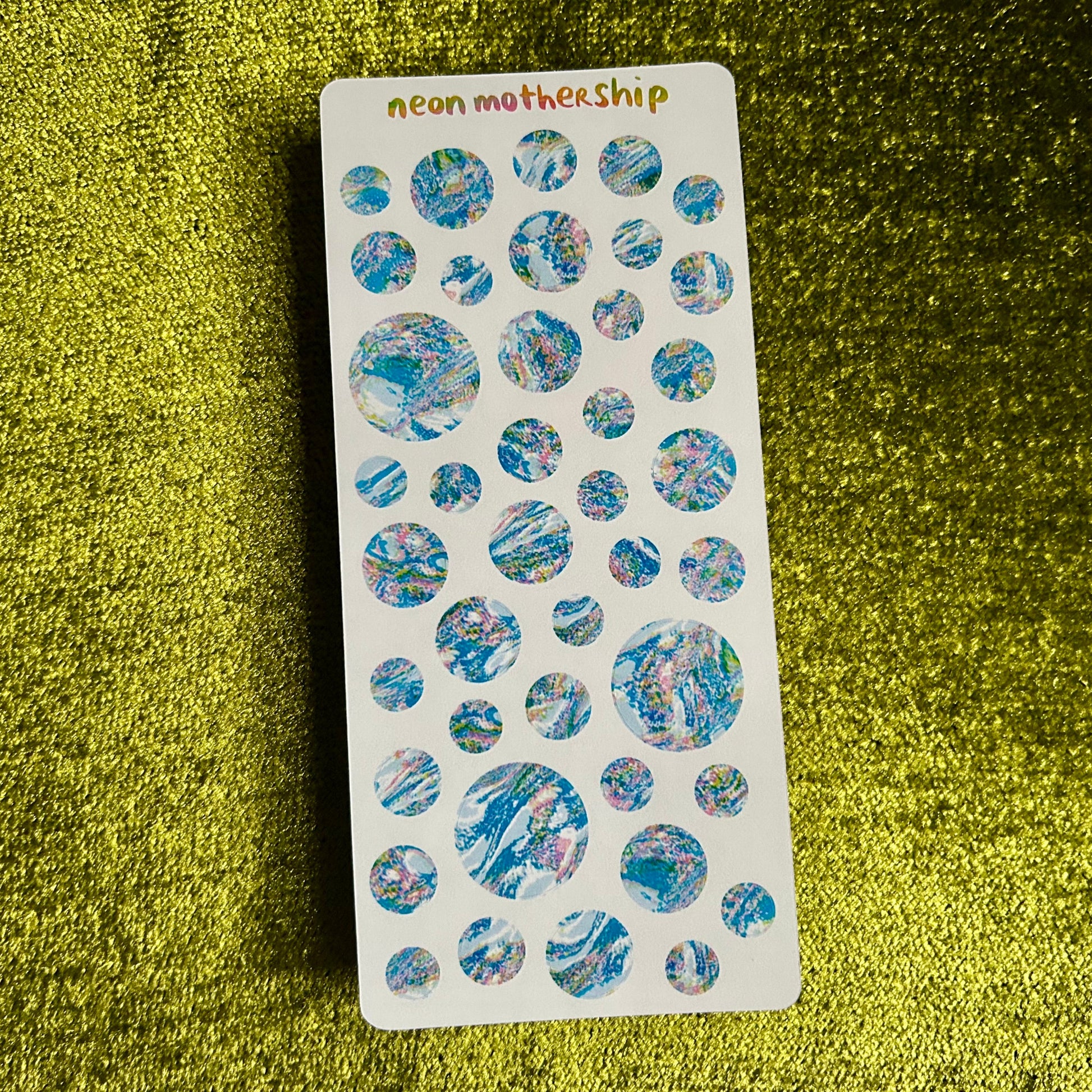 Sheet of round, multicolored stickers on a green textured surface with 'neon mothership' branding.
