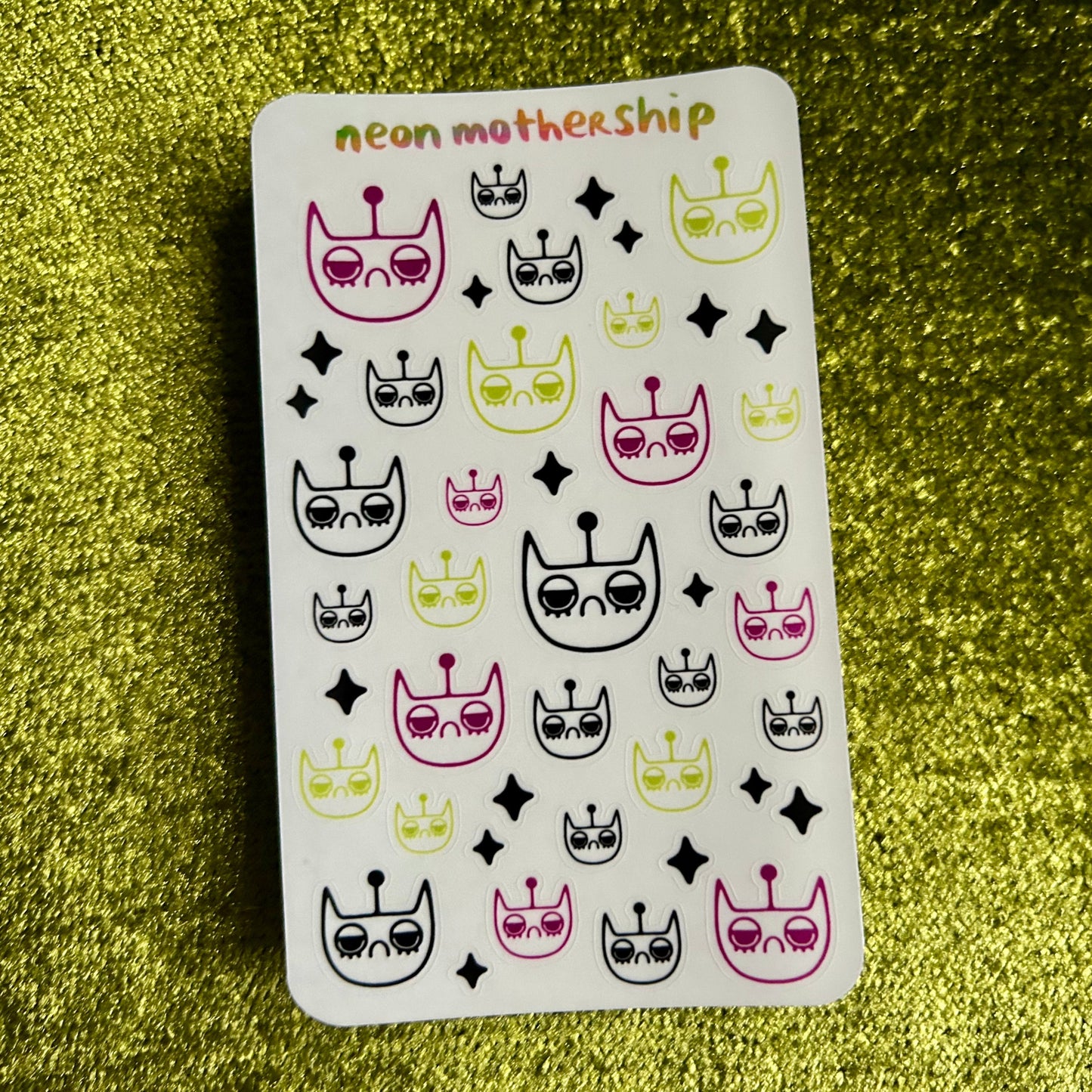 Sheet of stickers with cat-themed designs on a green textured background