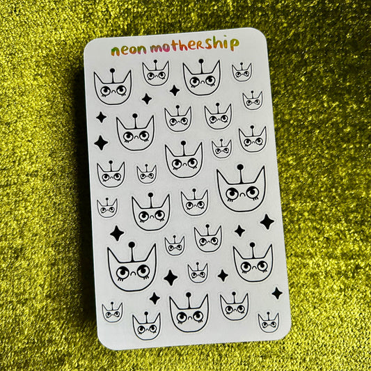 Sheet of black and white stickers with cat face designs on a green textured background