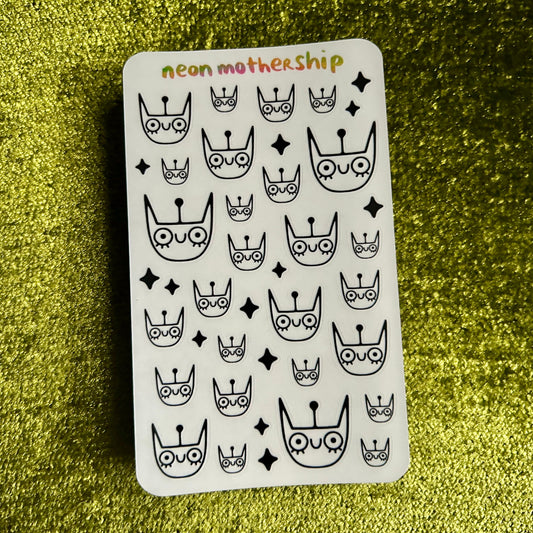 Sticker sheet with black and white cat designs on a green glittery background
