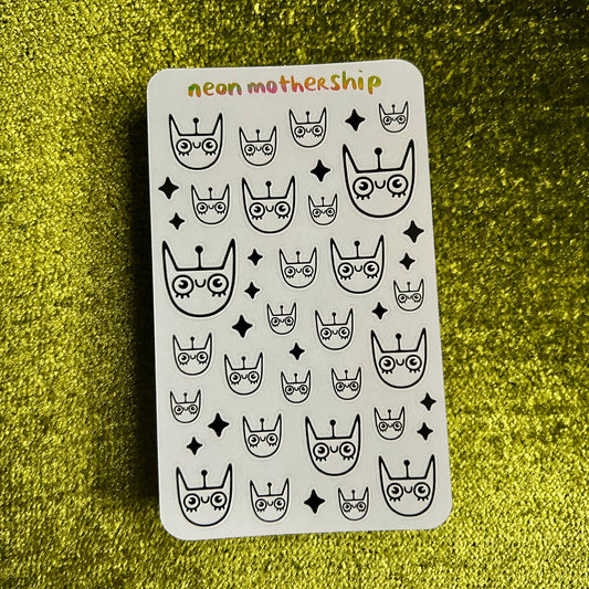 Sheet of black and white stickers with cat and crown designs on a green glittery background.