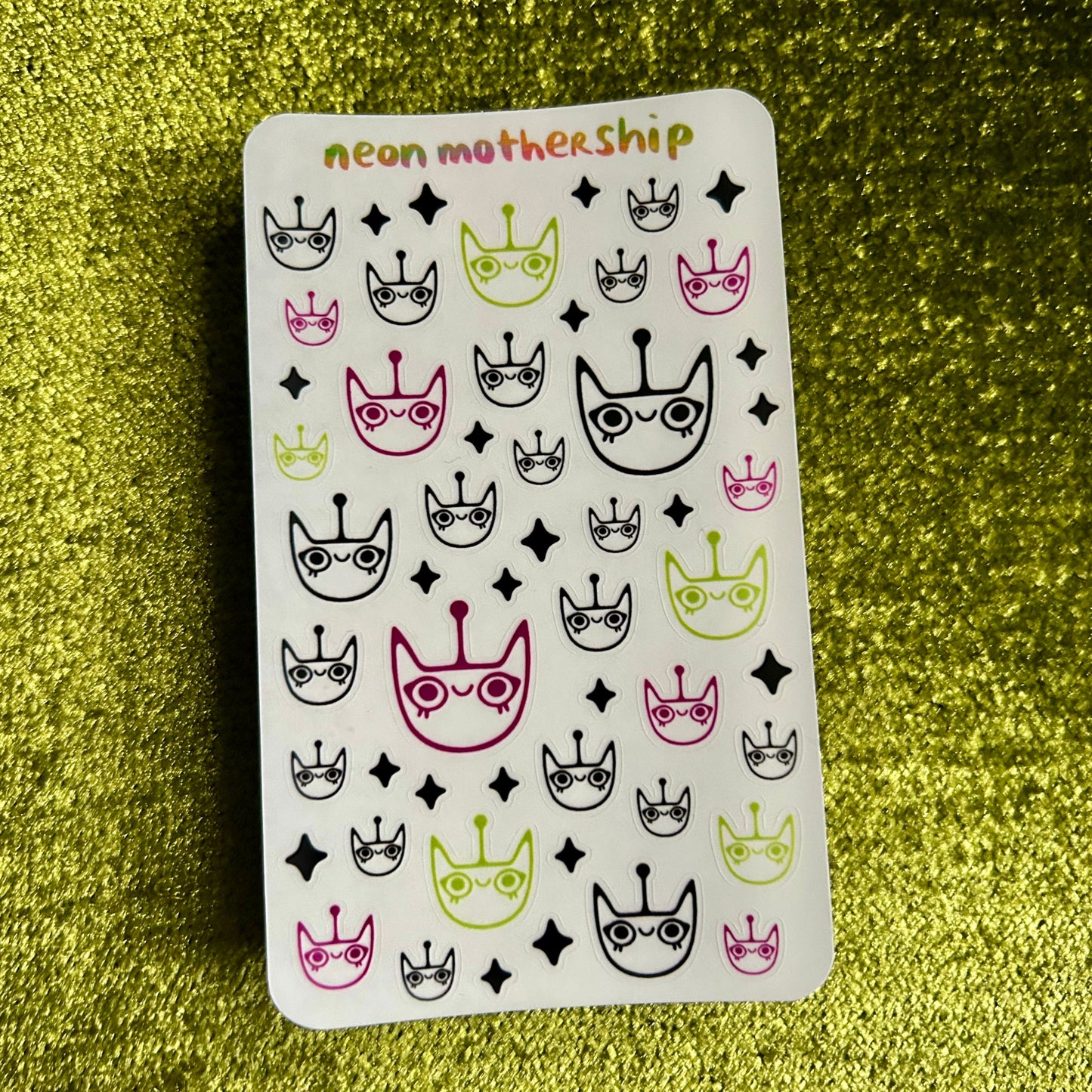 Sheet of stickers with cat and crown designs on a green textured background
