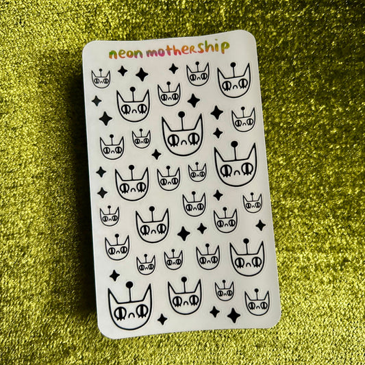 Sheet of black and white cat-themed stickers with 'neon mother ship' text on a green textured surface.