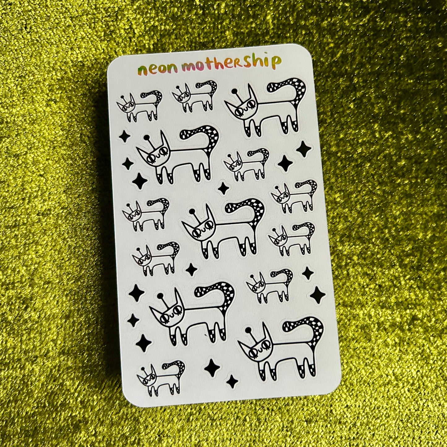 Sheet of black animal illustrations on a white card with 'neon mothership' branding, placed on a green textured surface.