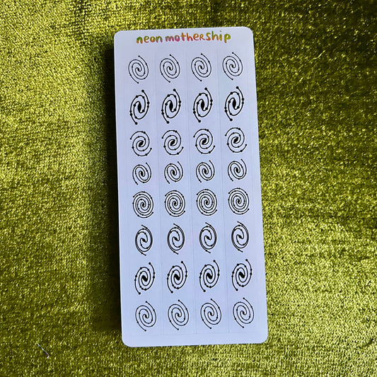 Sheet of black spiral patterns on a white card with 'neon motherhip' branding, placed on a green textured surface.
