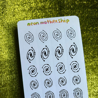 Sheet of black spiral stickers on a white card with 'neon mothership' branding, placed on a green textured surface.