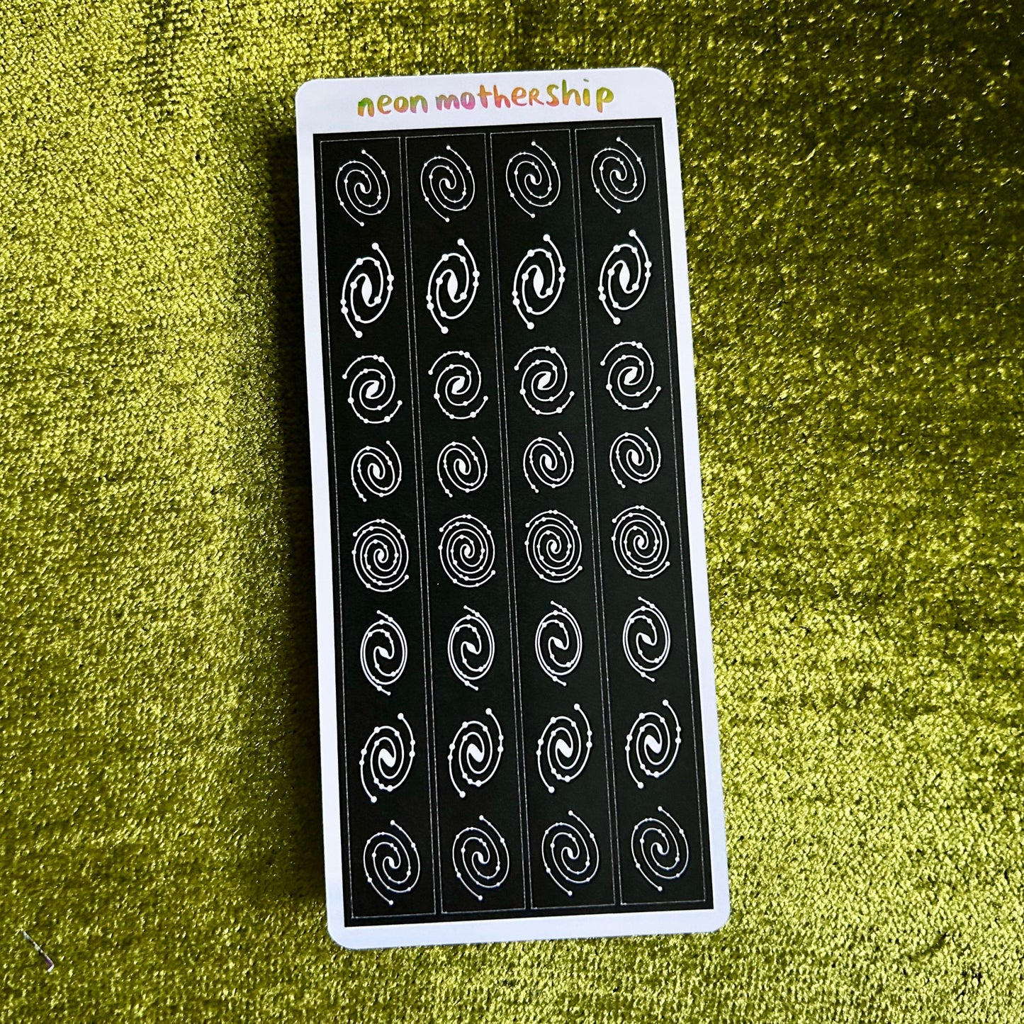 Sheet of black and white spiral pattern stickers on a green textured surface