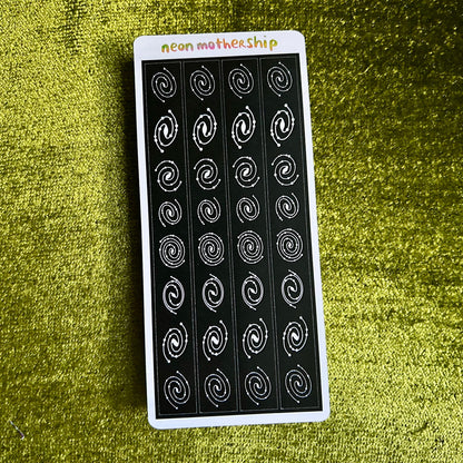 Sheet of black and white spiral pattern stickers on a green textured surface