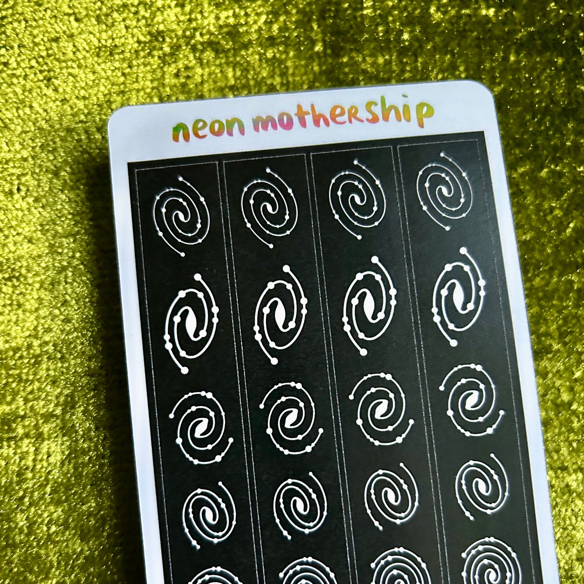 Sheet of white spiral stickers on a black background with 'neon mothership' branding on a green textured surface.