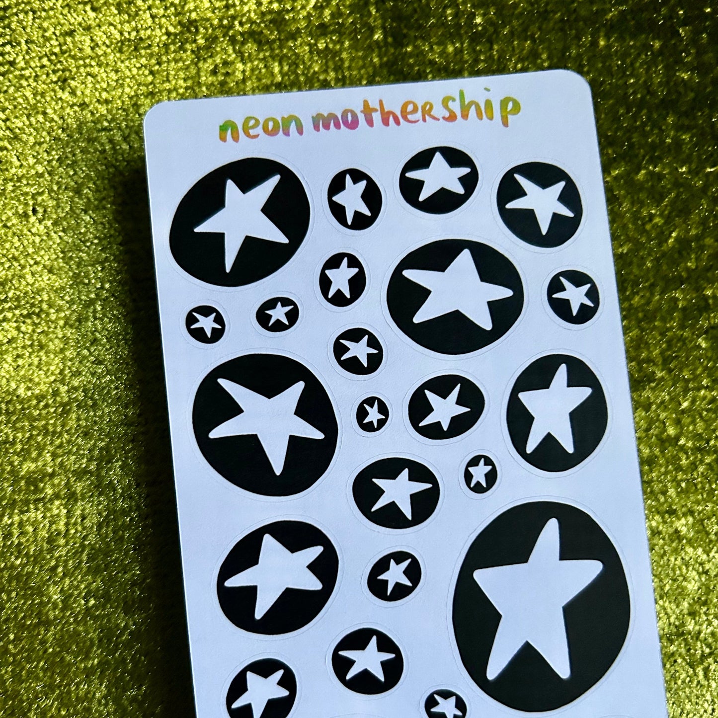 Sheet of star-shaped stickers with 'neon motherShip' branding on a green textured background