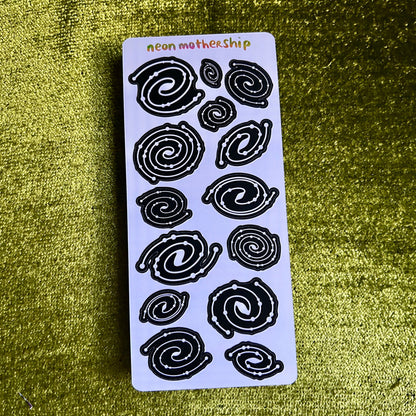 Sheet of black spiral stickers on a white card with 'neon mothership' branding, against a textured green background.