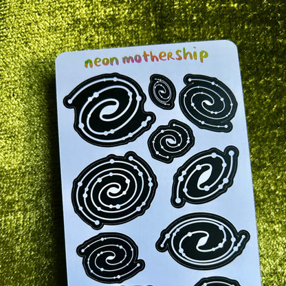 Sheet of black spiral designs on a light blue card with 'neon mothership' text, against a green textured background.