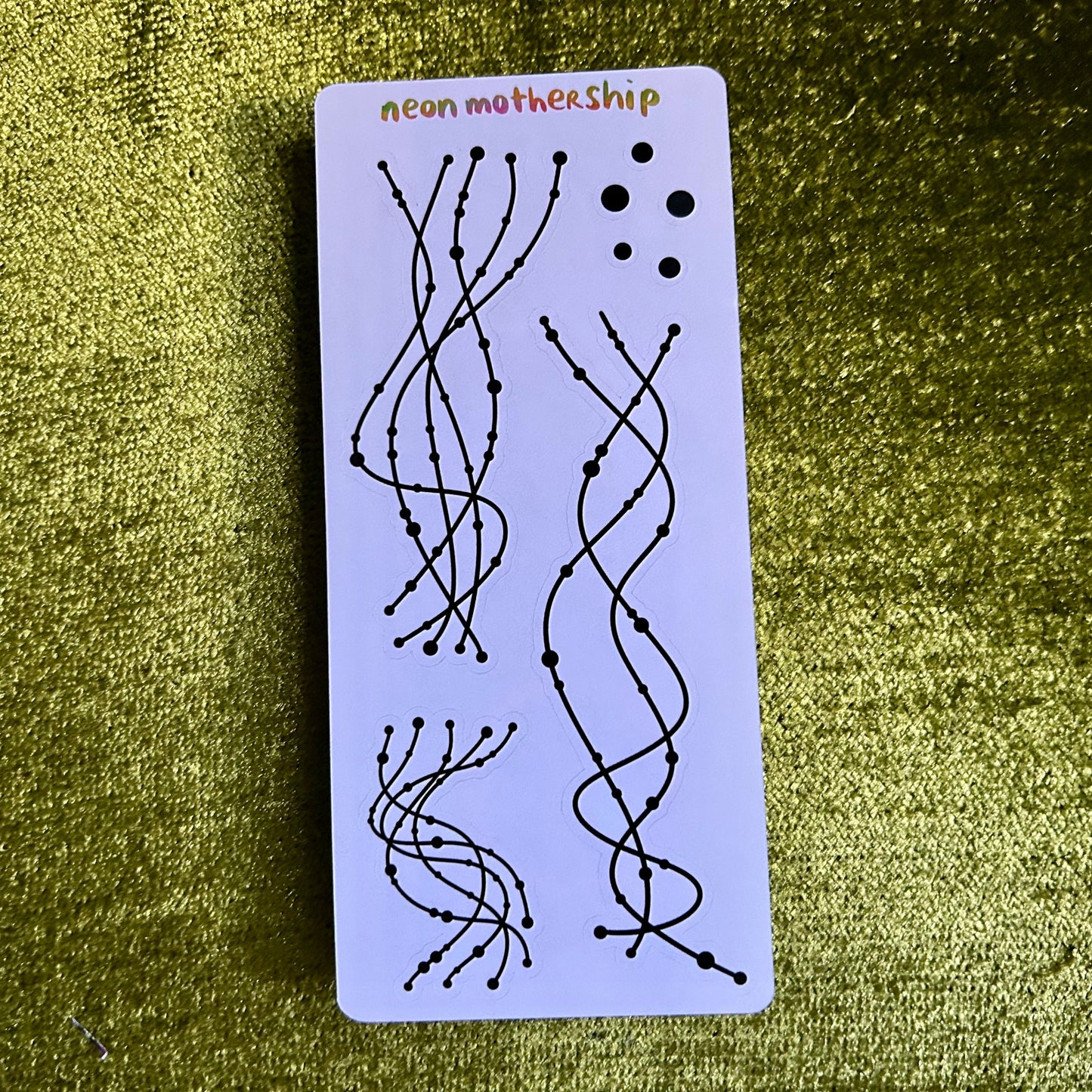 Rectangular card with black line art on a purple background, featuring the text 'neon mothership' on a green textured surface.