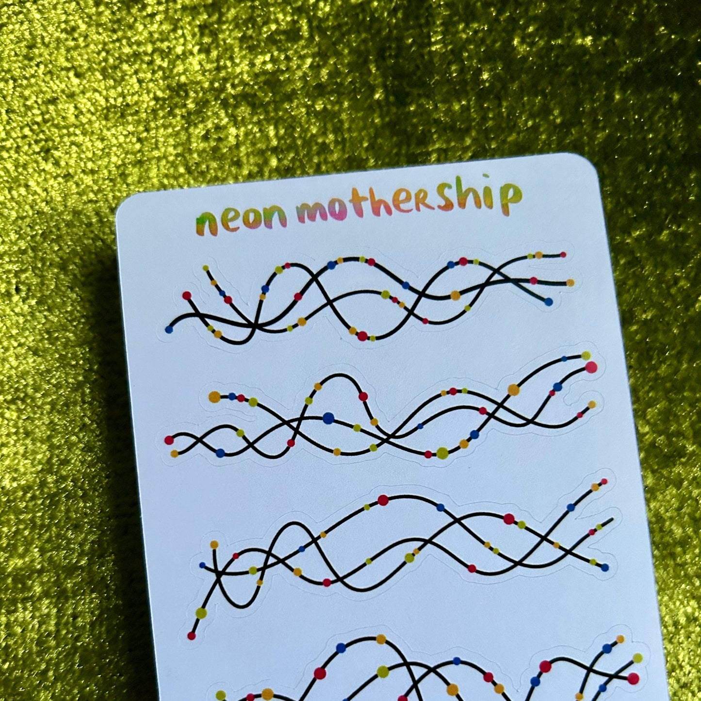 Card with colorful wavy sticker designs labeled 'neon mothership' on a green textured background