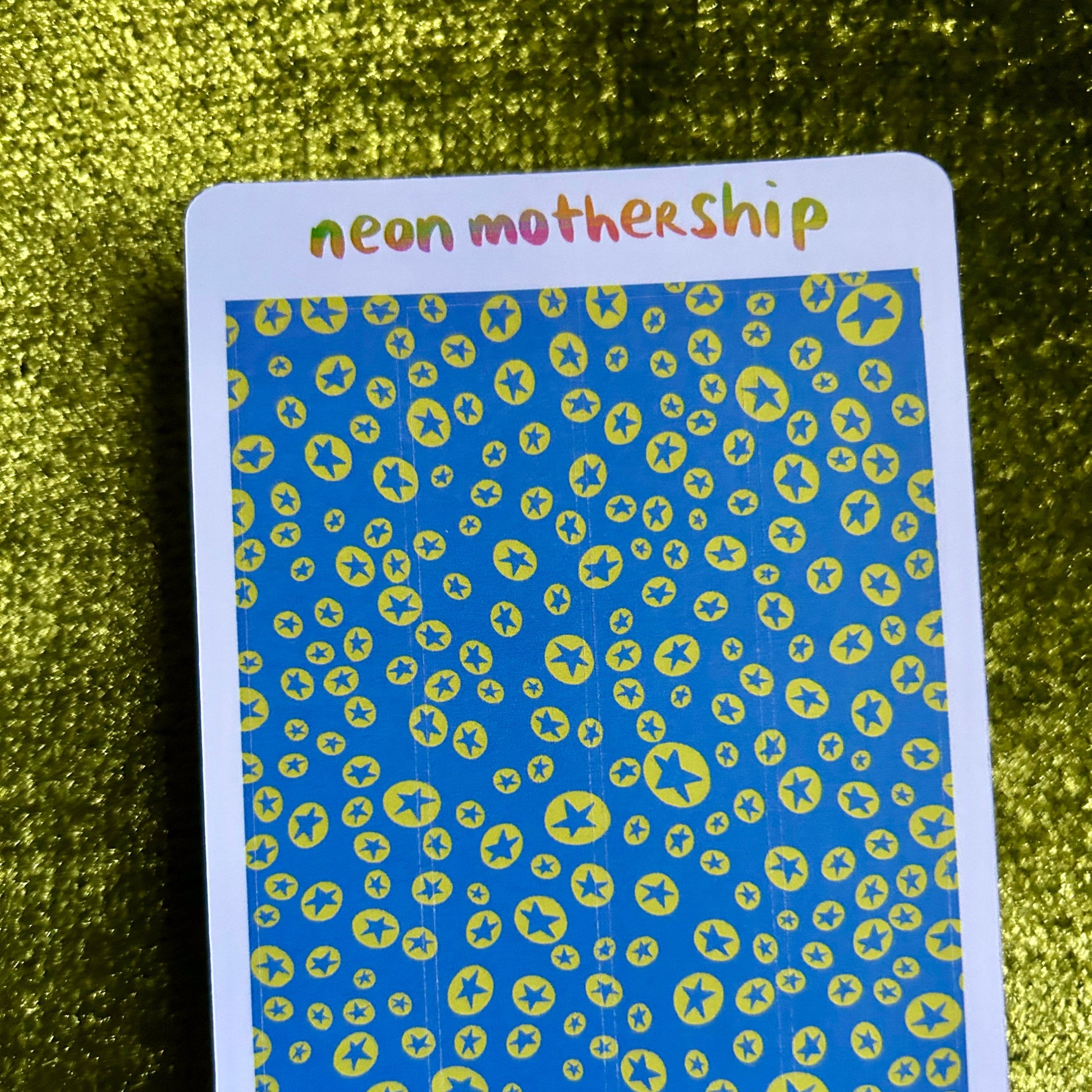 Card with 'neon mothership' text on a blue background with yellow patterns, against a green glittery background.
