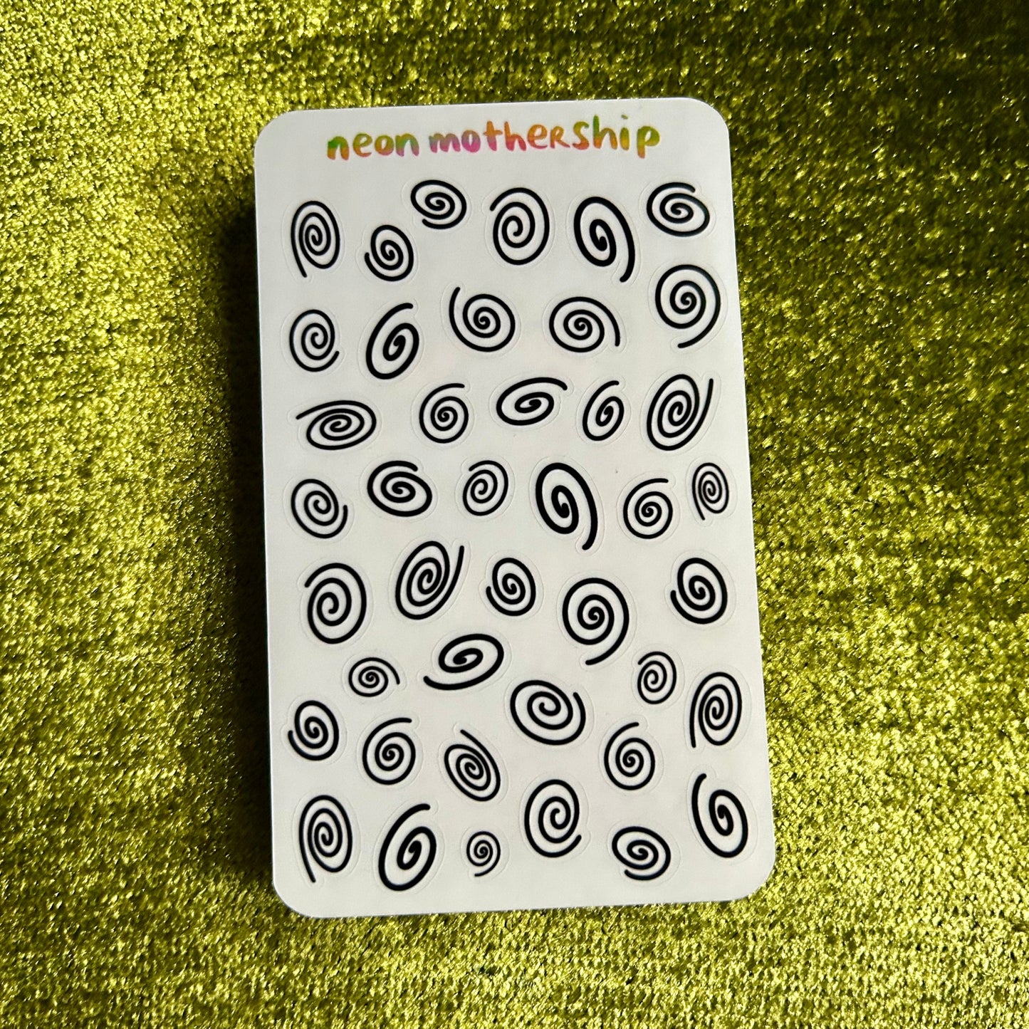 sticker sheet with black spiral patterns on a white background, placed on a textured green surface.