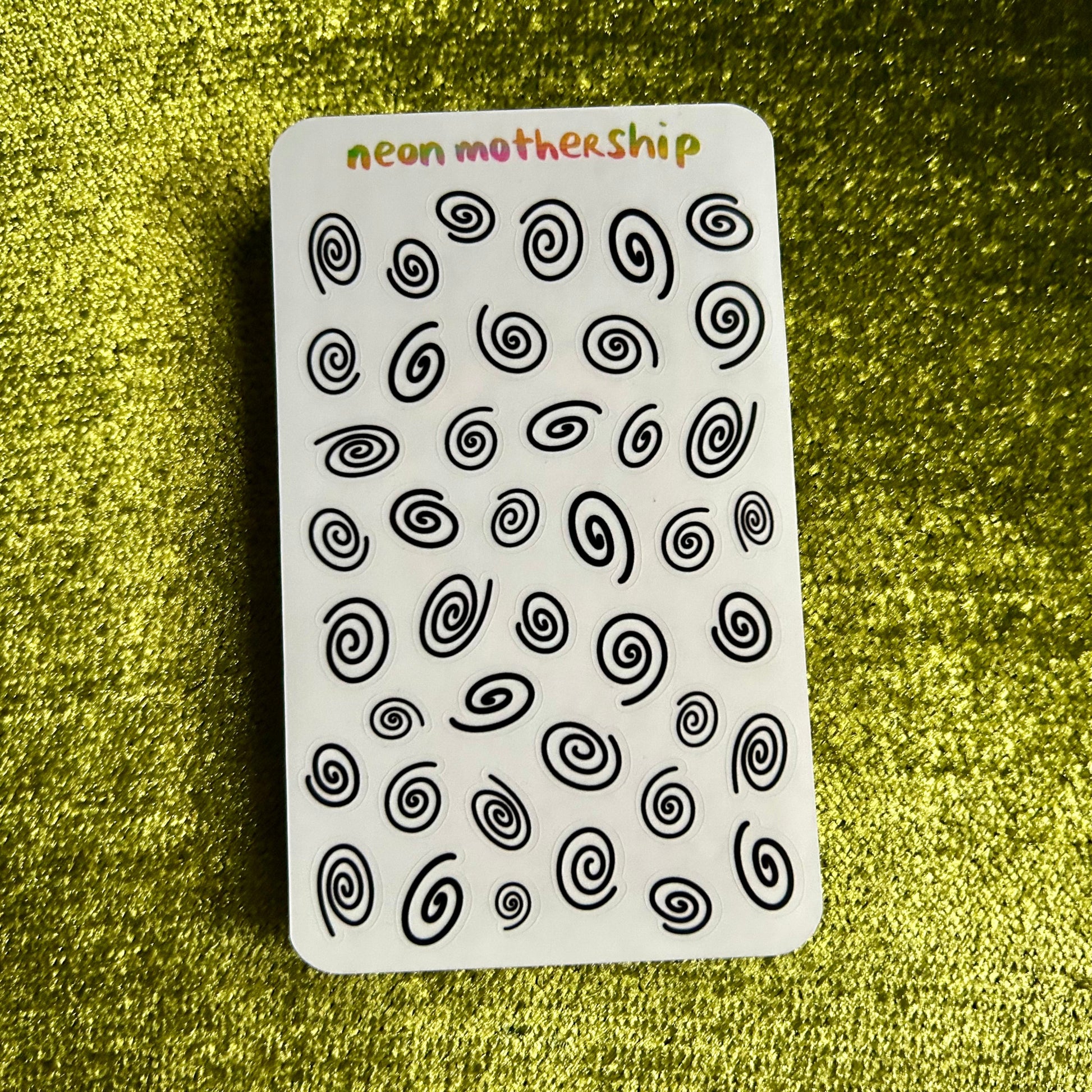 sticker sheet with black spiral patterns on a white background, placed on a textured green surface.