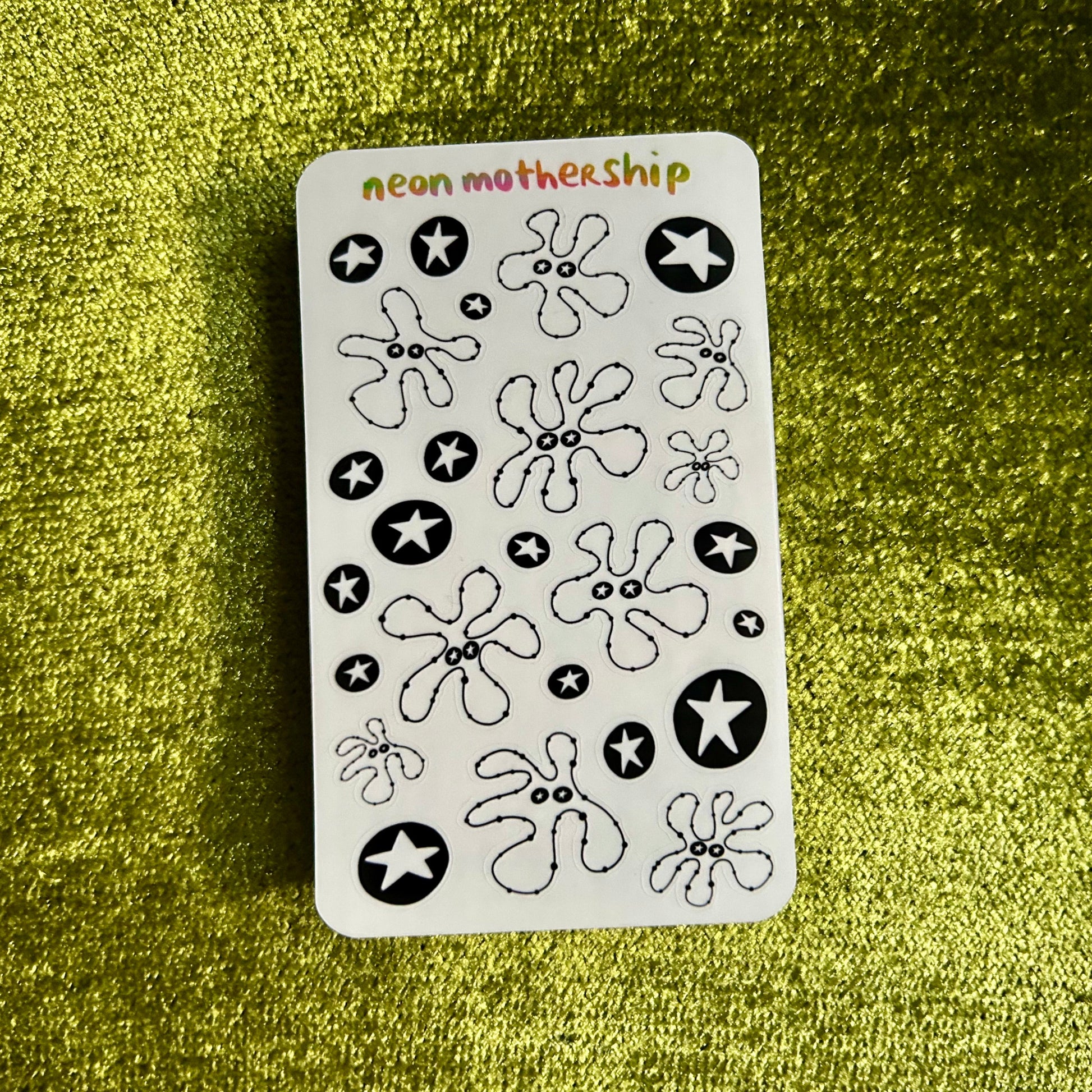 Sheet of black and white flower and star stickers on a green textured background