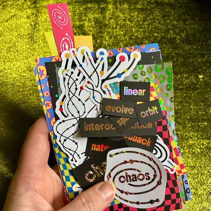 Hand holding a colorful pack of stickers with various designs and text on a green textured background.