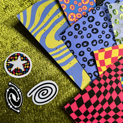 Colorful patterned paper sheets on a green textured surface with decorative stickers.