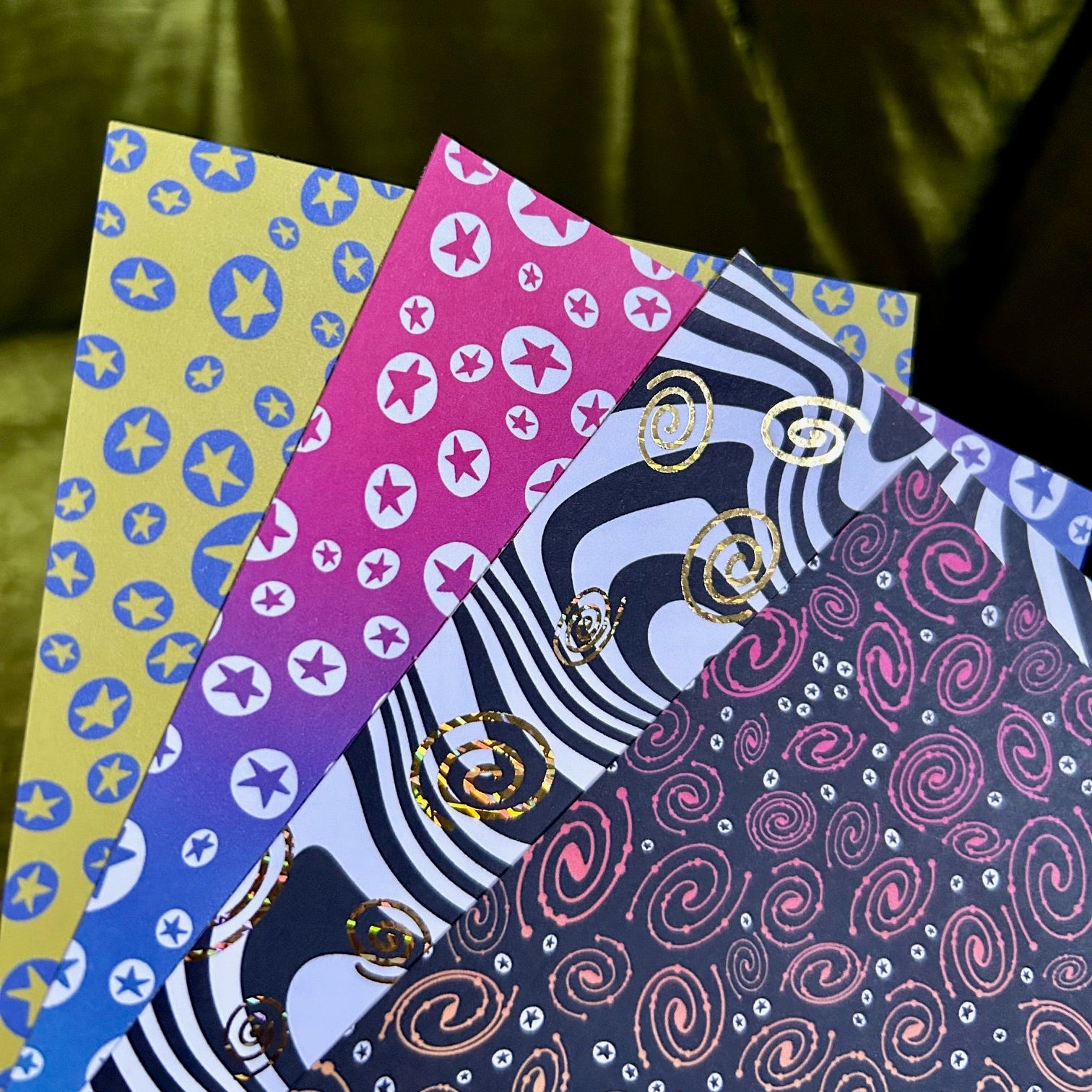 Four colorful patterned books stacked on a green fabric background