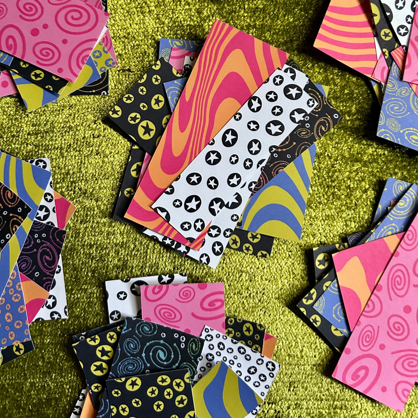 Colorful patterned paper pieces scattered on a textured green surface