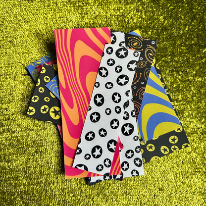 Five colorful patterned sticker scraps on a green textured surface