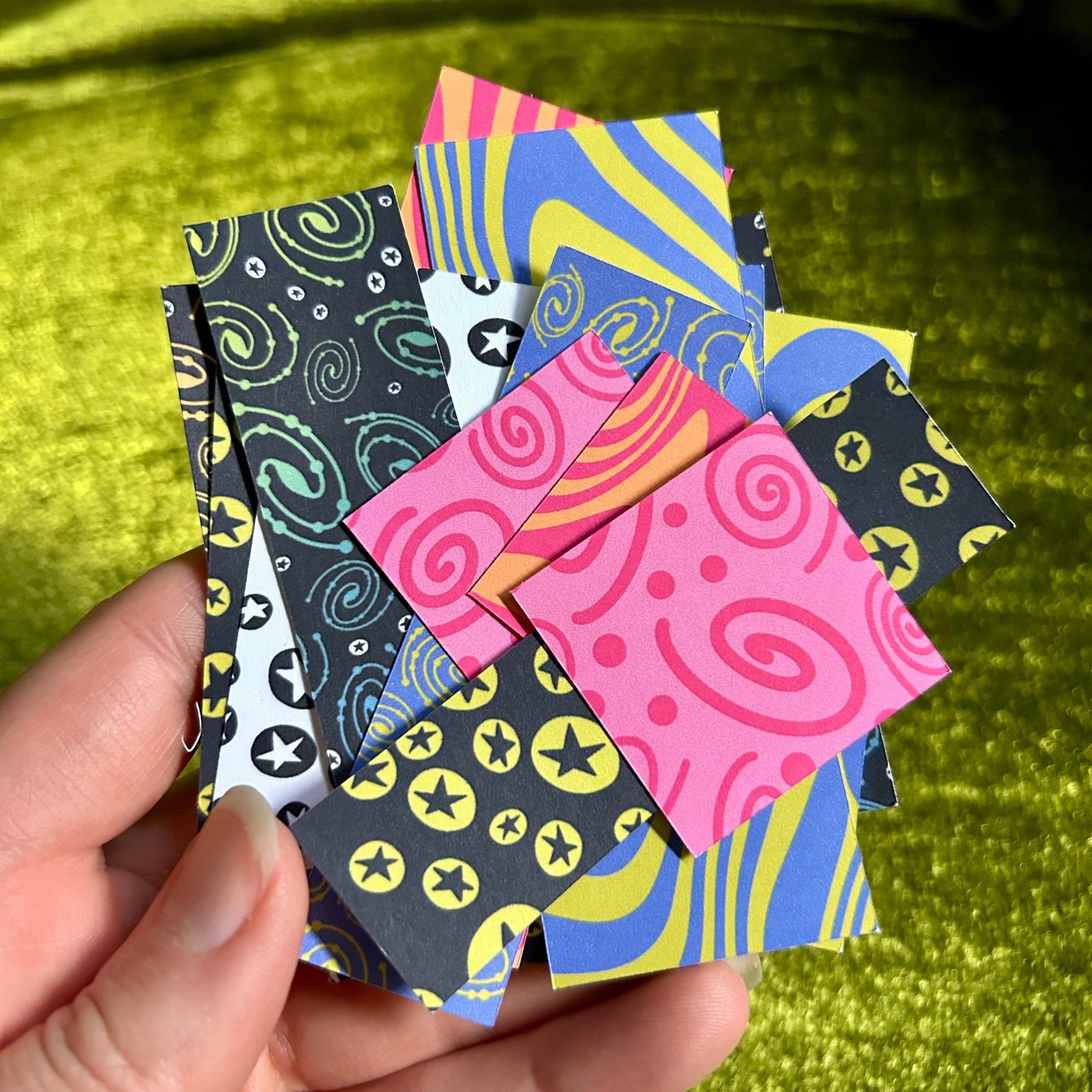 Hand holding colorful patterned paper squares against a green fabric background