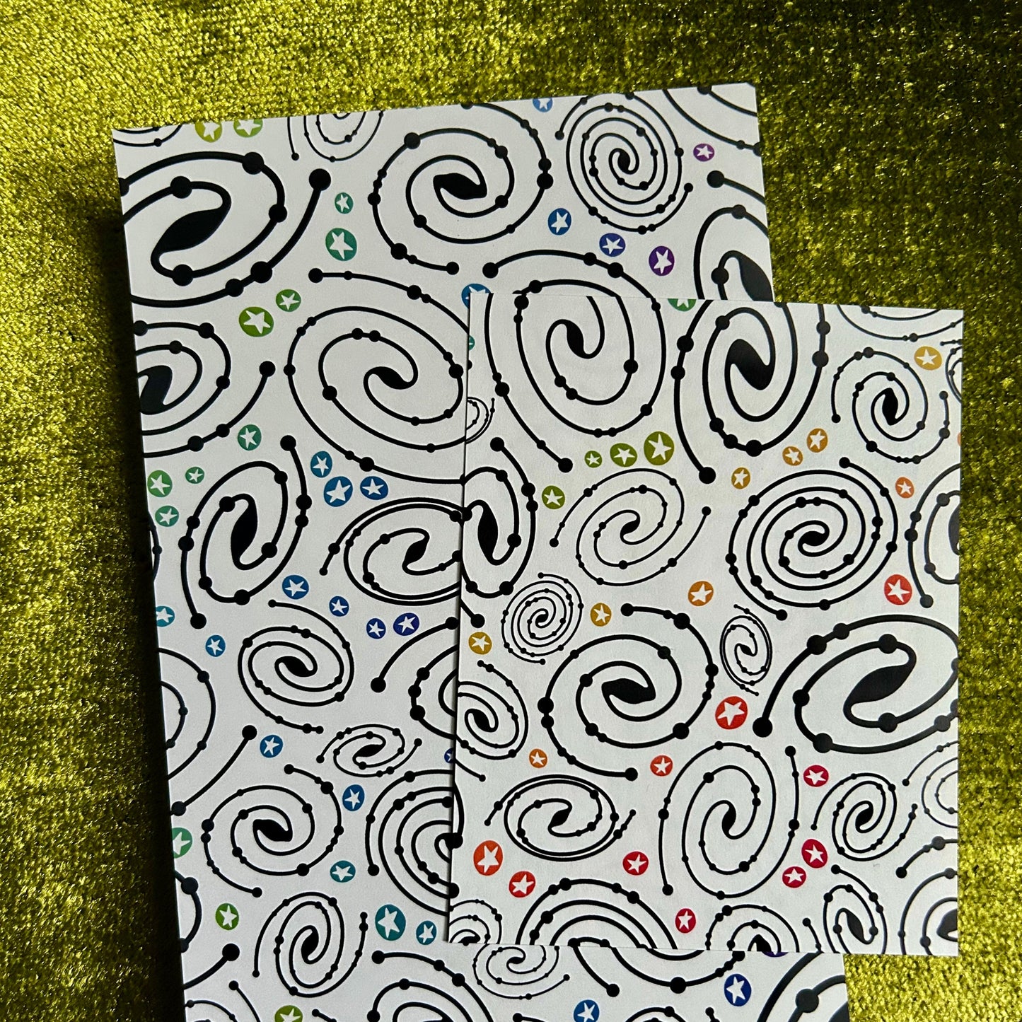 Two patterned notebooks with black swirl designs on a green textured background
