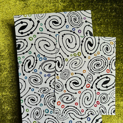 Two patterned notebooks with black swirl designs on a green textured background