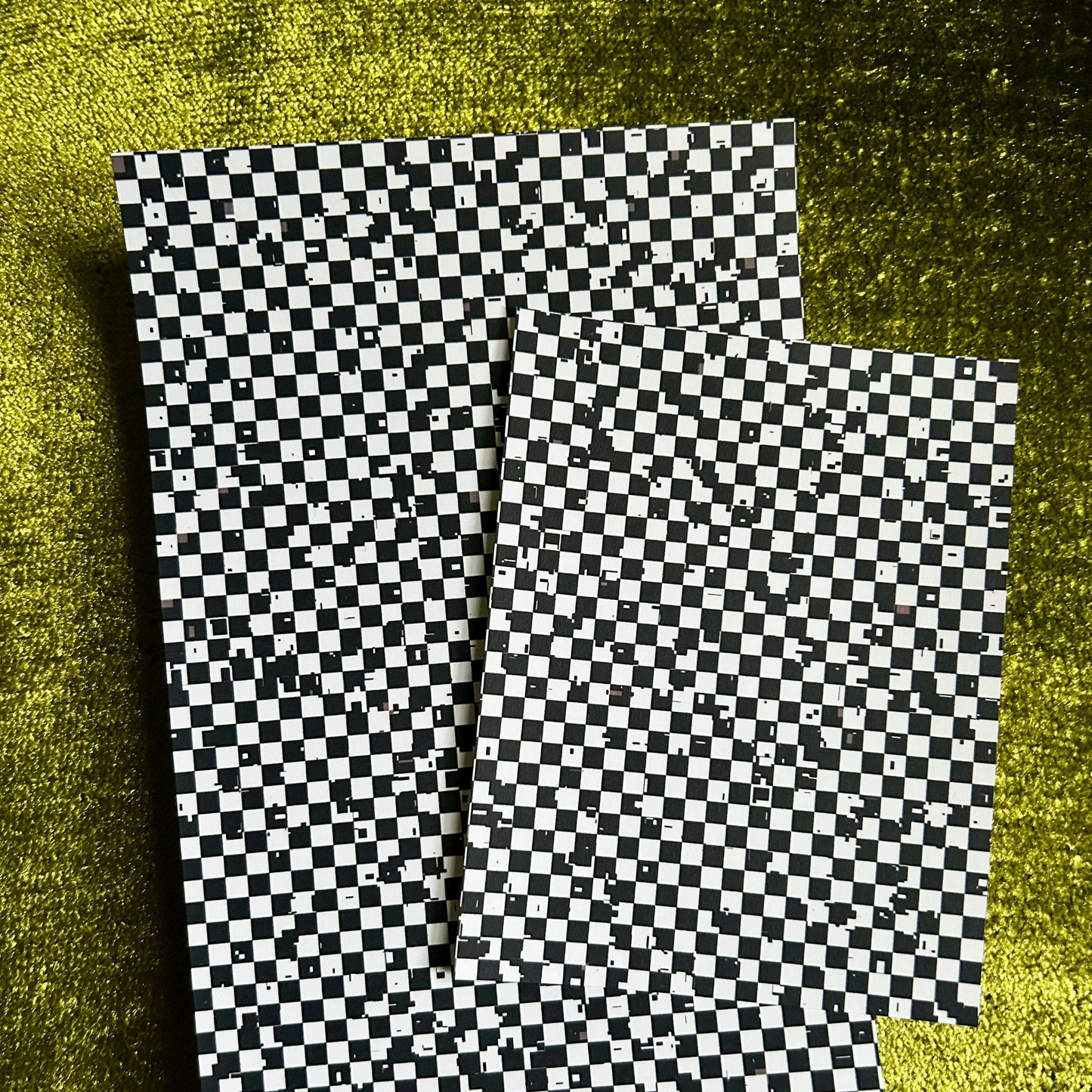 Two checkered paper sheets on a textured green surface
