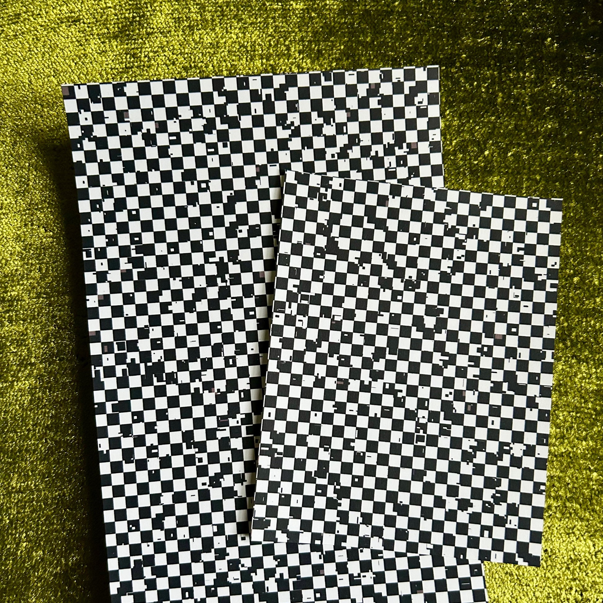 Two checkered paper sheets on a textured green surface
