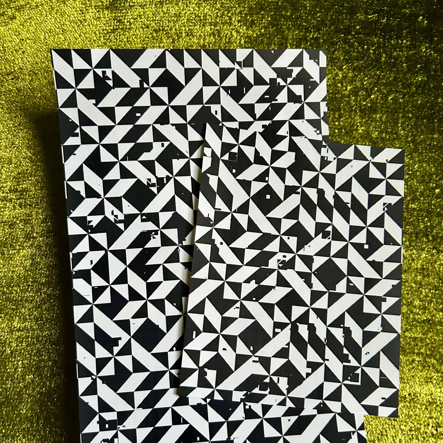 Two black and white patterned sticker sheets on a textured green surface