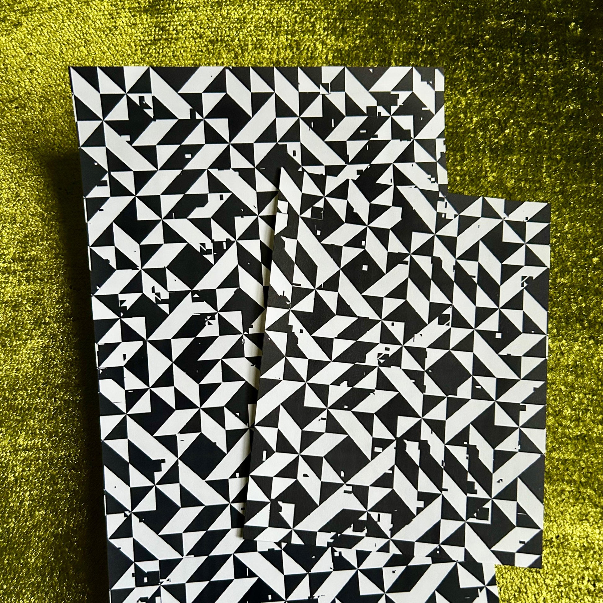 Two black and white patterned sticker sheets on a textured green surface