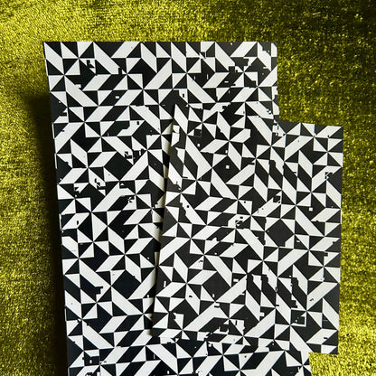 Two black and white patterned sticker sheets on a textured green surface