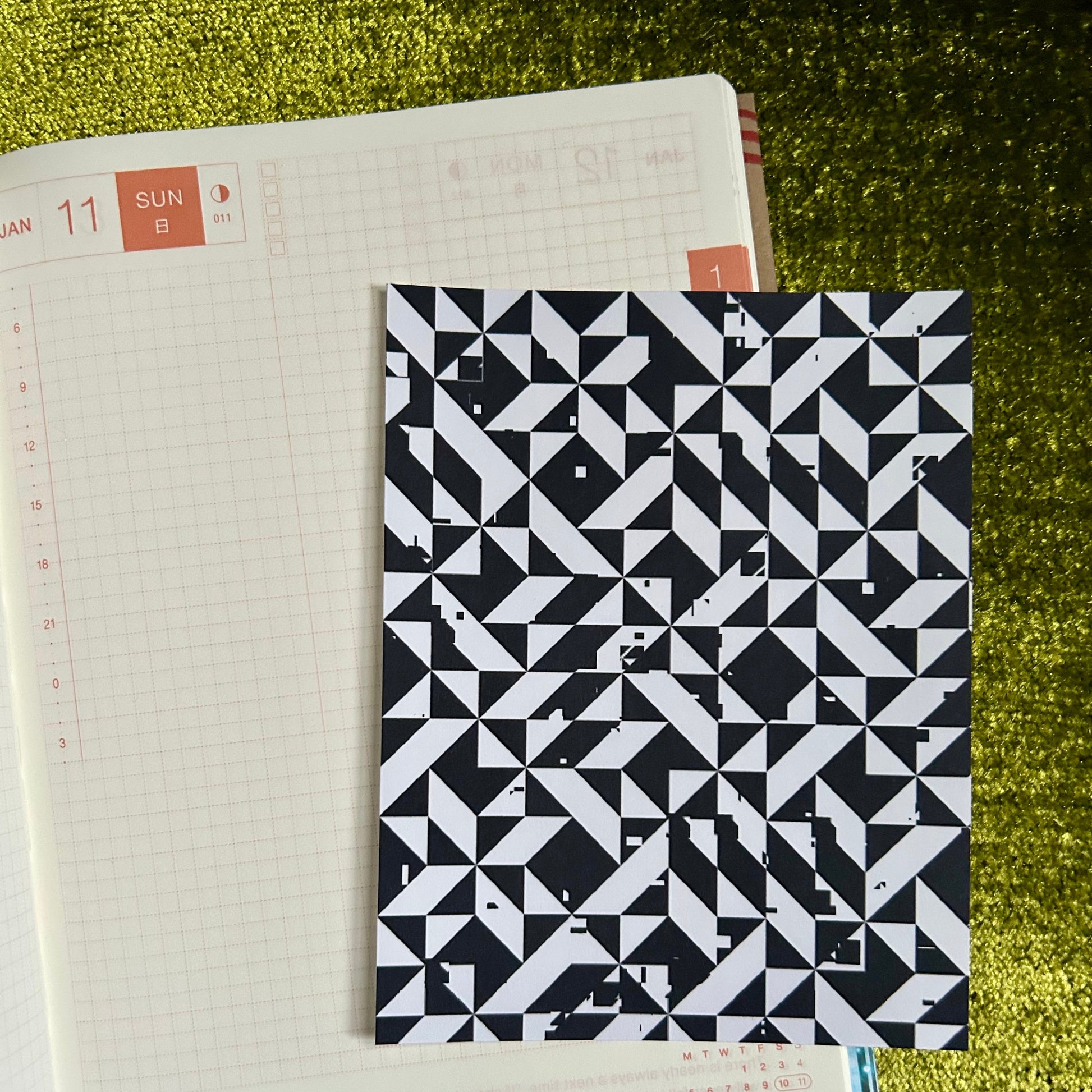 Notebook with a black and white geometric pattern sticker sheet on a green textured surface