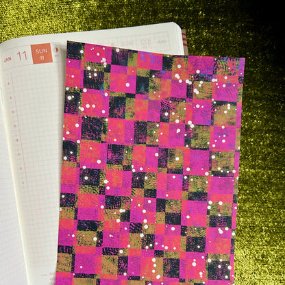 sticker paper with a colorful checkered cover on a green textured surface