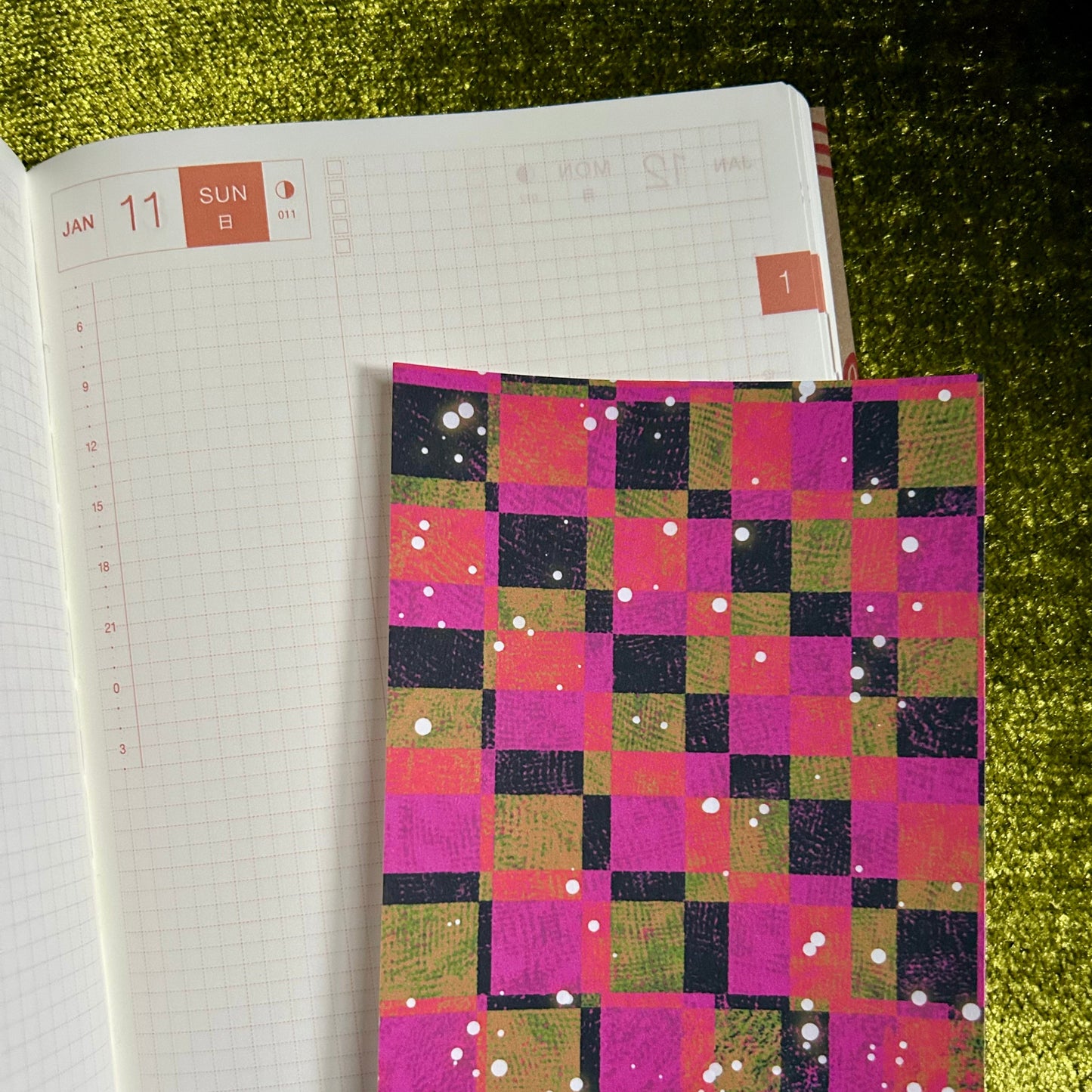Notebook with a colorful checkered sticker paper on top of an open planner.