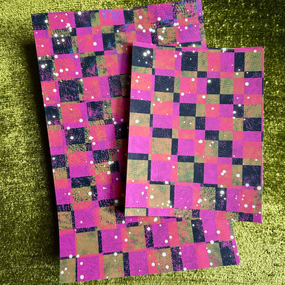Two pieces of checkered sticker paper with a pink and purple pattern on a green textured background