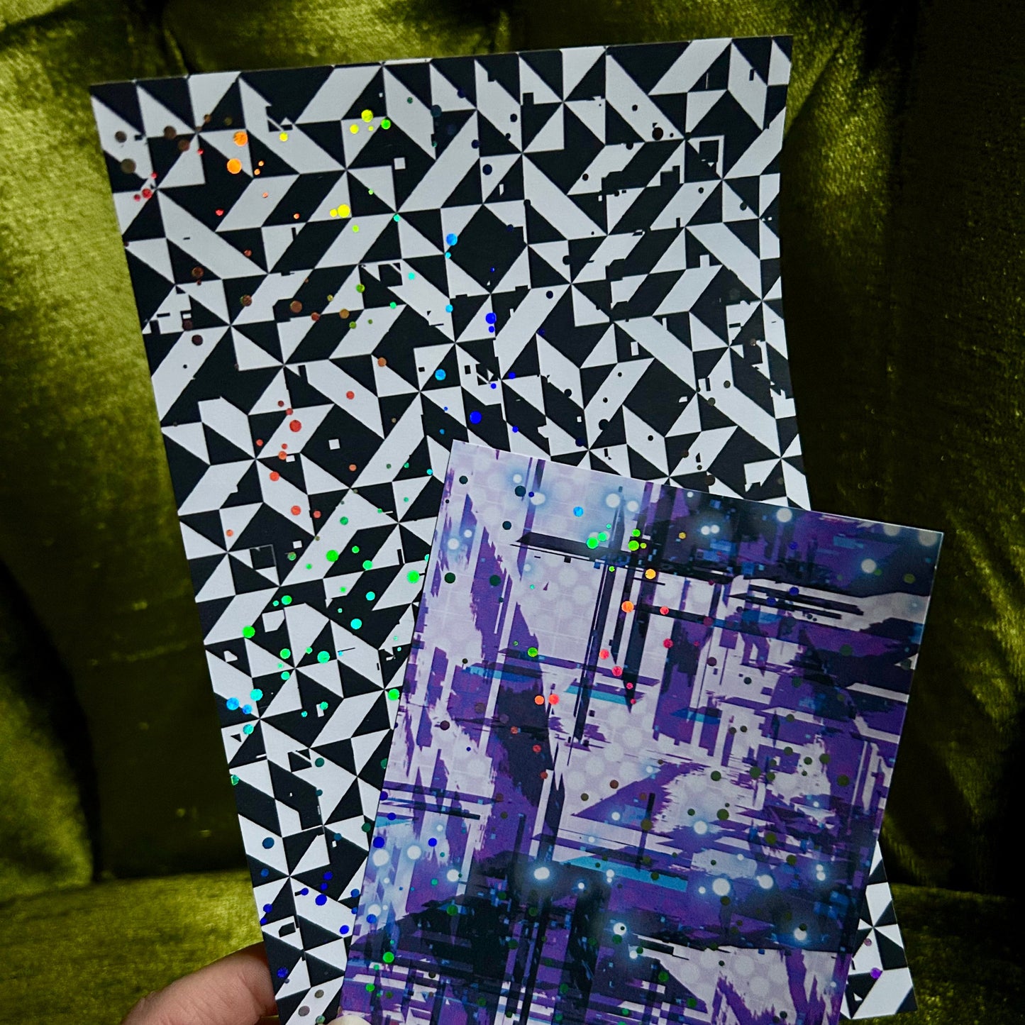 Two geometric-patterned sticker sheets held against a green fabric background
