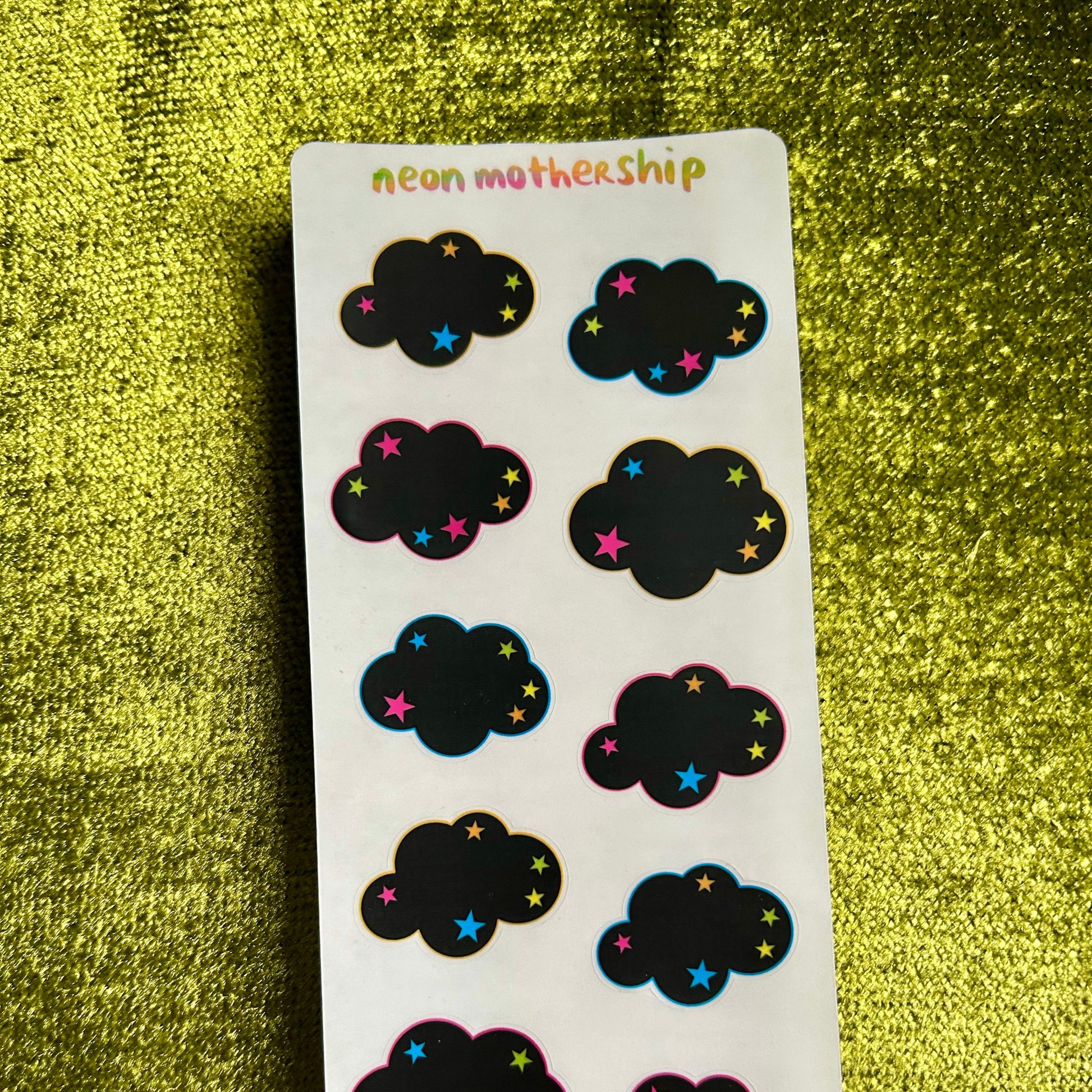 Sheet of cloud-shaped stickers with colorful stars on a green textured surface
