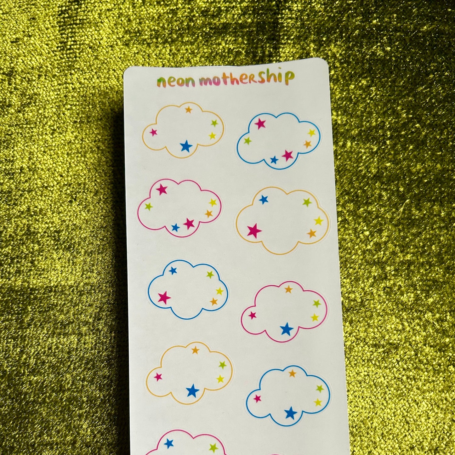 Sheet of cloud-shaped stickers with colorful stars on a green textured background