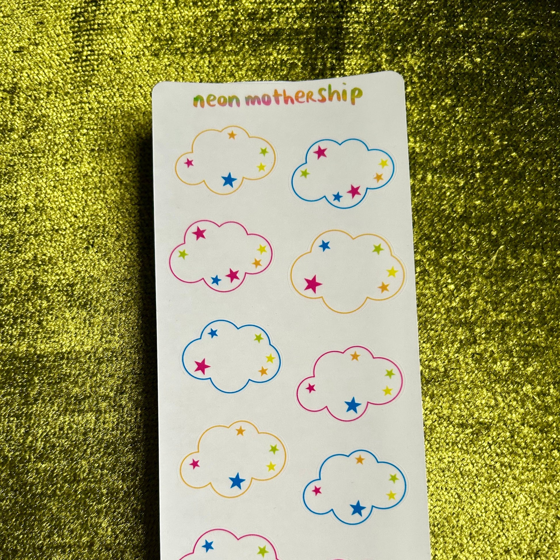 Sheet of cloud-shaped stickers with colorful stars on a green textured background