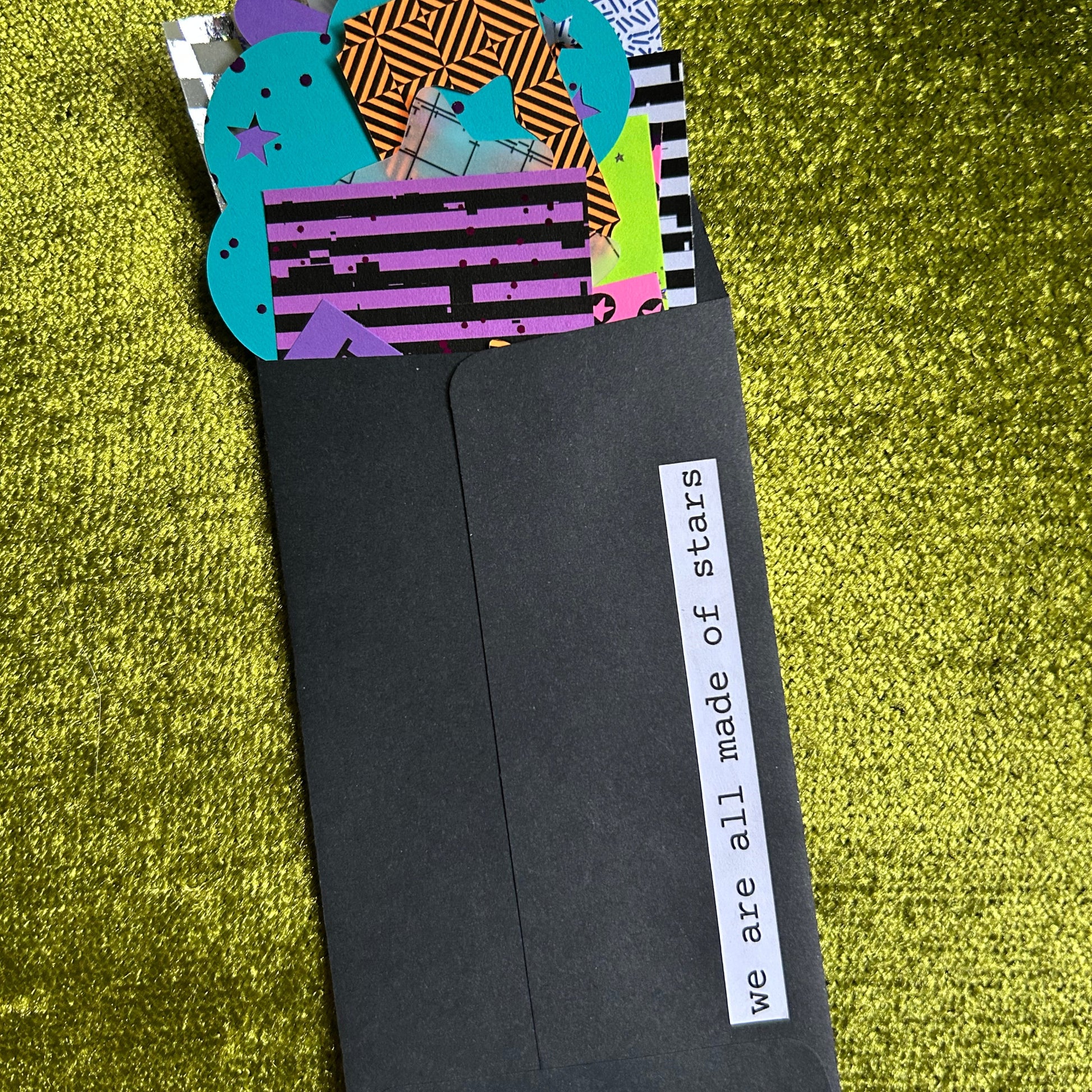 Black envelope with colorful stickers on a green textured surface