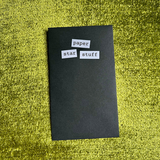 small black envelope with paper star stuff on the front against a green textured background
